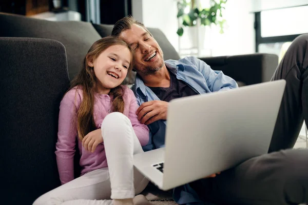 Happy father and daughter having fun while surfing the net on laptop in the living room. 