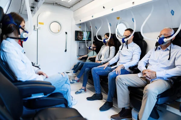 Group of mixed age people wearing masks while having oxygen therapy in hyperbaric chamber.