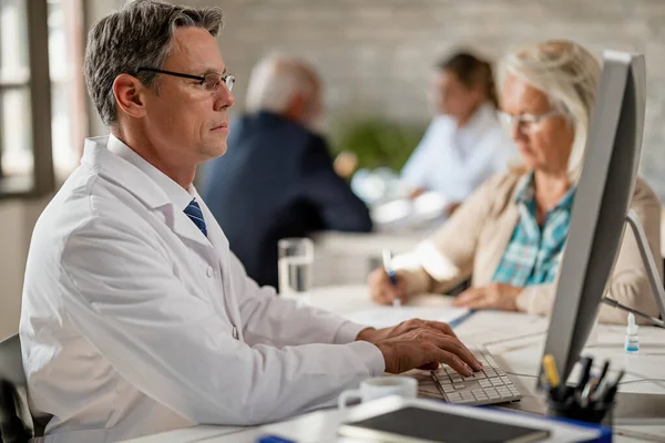 Male Doctor Working Computer While Having Meeting Senior Patient Clinic — Foto de Stock