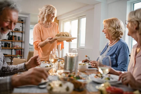 Happy Senior Woman Serving Bread While Talking Her Friends Dining — Foto Stock