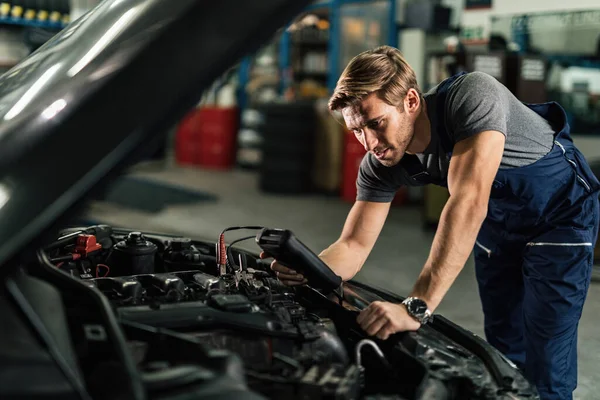 Young auto mechanic doing engine diagnostic while working in repair workshop. 