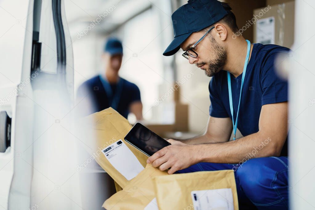 Young worker using digital tablet and scanning bar code on a label of a package in a delivery van. 