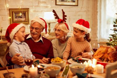 Happy senior couple enjoying in conversation with their grandchildren during family lunch on Christmas at dining table.