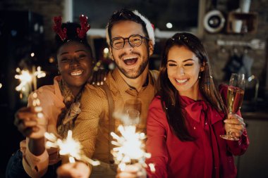 Group of happy friends having fun with sparklers while drinking Champagne and celebrating New Year at home. 