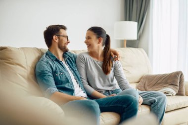 Happy woman and her husband communicating while relaxing in the living room.