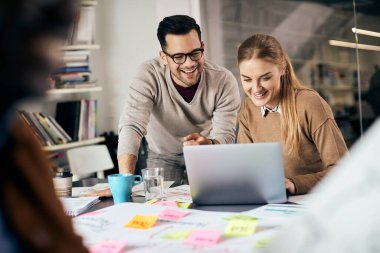 Happy creative businessman and his female colleague using laptop while working at casual office. 