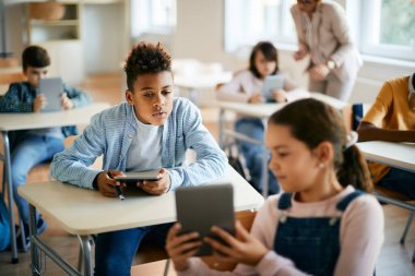 African American schoolboy and his classmate using touchpad during computer class in the classroom. 