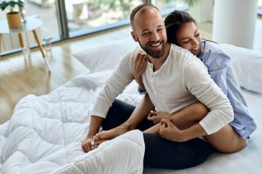 Young happy couple sitting embraced on a bed and having fun in the morning. 