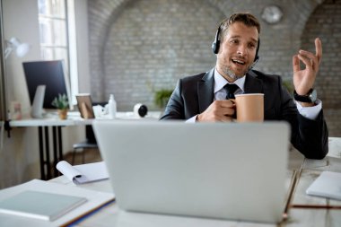 Male entrepreneur drinking coffee while having video call over computer in the office. 