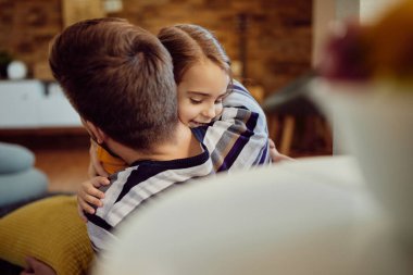 Affectionate father and daughter embracing while relaxing at home. Focus is on little girl.