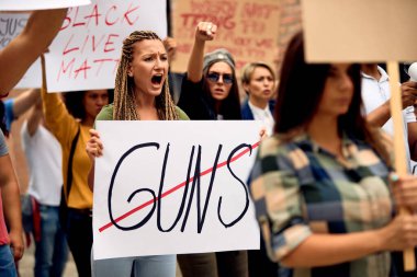 Young Caucasian woman shouting while marching for human rights with crowd of people through city streets. 