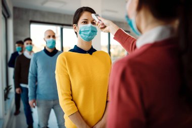 Female entrepreneur coming to a business seminar and getting her body temperature measured due to coronavirus pandemic. 
