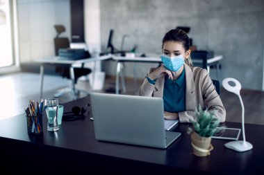 Young businesswoman wearing face mask while using computer and working in the office. 