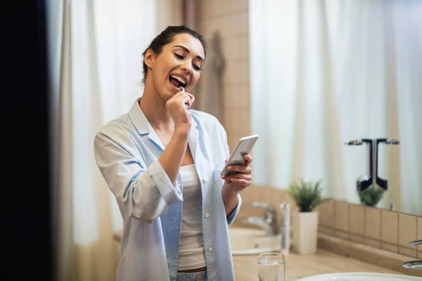 Молода Усміхнена Жінка Чистить Зуби Читає Текстове Повідомлення Мобільному Телефоні — стокове фото