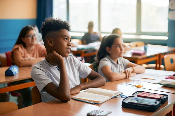 Group of elementary students learning on a class at school. Focus is on smiling black boy.