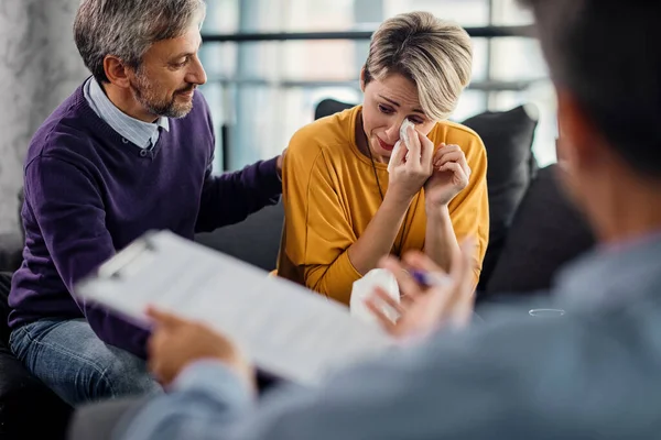 Mid adult couple having psychotherapy with marriage counselor in the office. Focus is on crying woman.