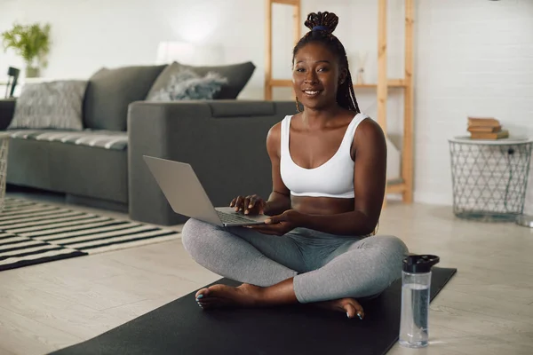 Young lack athletic woman using laptop during home workout at looking at camera.