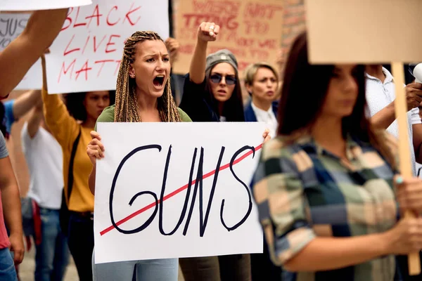 Young Caucasian woman shouting while marching for human rights with crowd of people through city streets. 