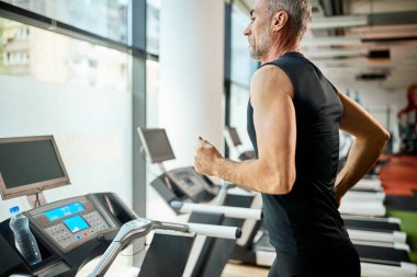 Spor salonunda spor yaparken koşu bandında koşan olgun bir sporcu.. 