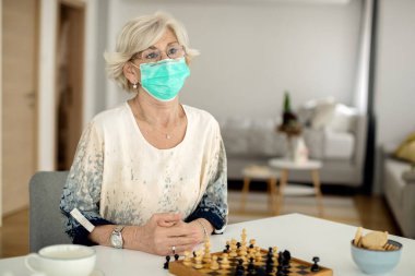 Pensive senior woman with protective face mask feeling lonely during home quarantine due to coronavirus epidemic. 