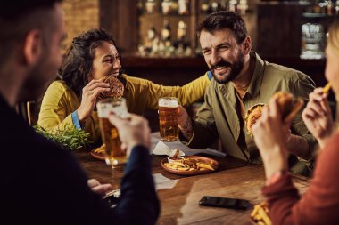 Happy man having fun with his friends while drinking beer and eating burgers in a pub. 
