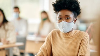 Portrait of black female student with face mask attending a class at the university and looking at camera. 