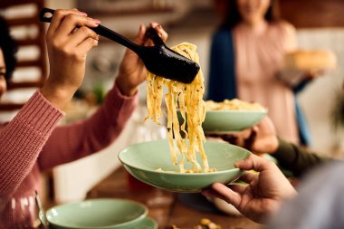 Close-up of unrecognizable adult eating pasta for lunch at dining table at home. 