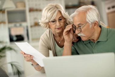 Senior man and his wife using laptop while going through their finances at home.