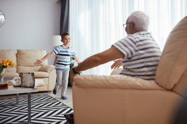 Happy kid with arms outstretched running in grandfather's embrace in the living room.