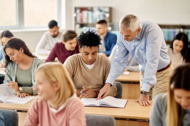 Mature professor assisting African American student with a lecture in the classroom.
