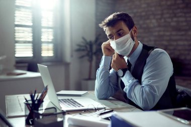 Young businessman wearing protective face mask while working in the office during coronavirus pandemic. 
