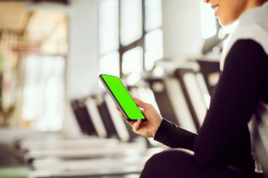 Close-up of athletic woman using mobile phone during sports training in a gym. Copy space. 