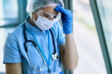 Exhausted female doctor having headache while working at clinic during coronavirus epidemic. 
