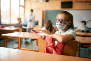 Elementary student looking at camera during a class and wearing face mask due to coronavirus pandemic. 