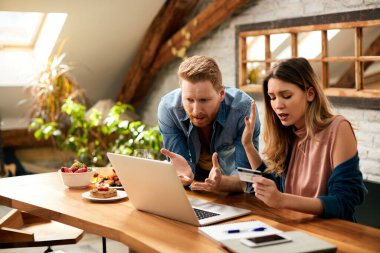 Displeased couple arguing while looking at their online bank account on laptop at home. 