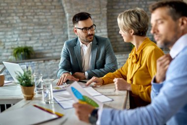 Real estate agent talking to a couple while analyzing blueprints during the meeting in the office. 