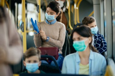 Woman putting on protective gloves while wearing face mask and commuting withr son by public transportation. 