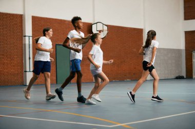 Full length of elementary students running while having PE class at school gym.