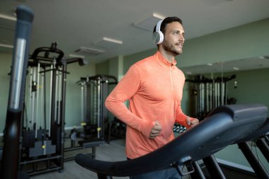 Young smiling athlete running on treadmill while working out in a health club. 