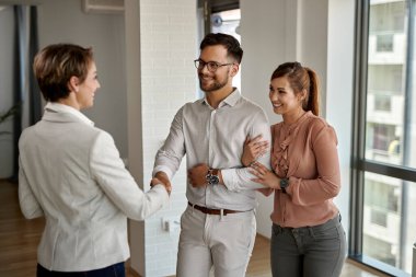 Young happy couple shaking hands with real estate agent while buying a new apartment. 