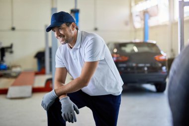 Happy car mechanic resting while working in auto repair shop. 