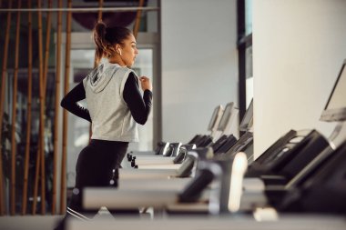 Side view of athletic woman exercising on running track while working out at health club.