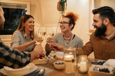 Group of cheerful friends toasting with wine while having dinner in dining room.