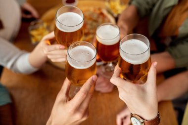 Close-up of friends celebrating and toasting with beer in a pub. 