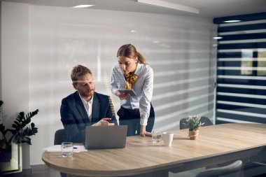 Young businesswoman and her male colleague reading an e-mail on laptop while working together the office The view is through the glass. 