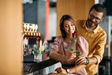 Romantic man surprising his girlfriend with red rose on Valentine's day in a cafe.