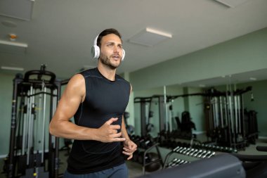 Young athlete running on a treadmill while listening music on headphones at health club.