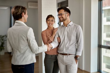 Happy couple buying a new home and handshaking with their real estate agent. 