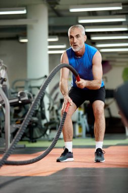 Dedicated mature athlete sportsman uses battle ropes during cros