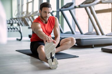 Male athlete doing relaxation exercises while warming up for sports training in health club.